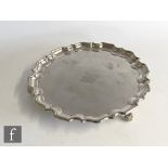 A hallmarked silver circular salver raised on four scroll feet with central engraved crest within