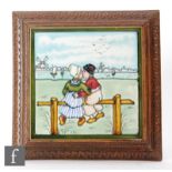 A framed 8in tile decorated with a tubelined Dutch scene with a lady and gentleman kissing whilst
