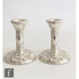 A pair of hallmarked silver Edwardian style piano candlesticks with embossed foliate decoration to