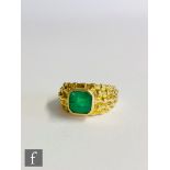 An 18ct emerald ring central canted square cut collar set stone to a wide rough finished shank,