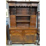 An 18th Century and later oak dresser with plate rack, with a shaped cornice, two small cupboards,