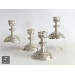 A composed set of four hallmarked silver squat candlesticks with part embossed foliate decoration to