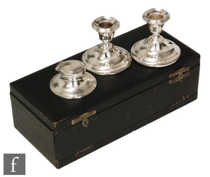 A cased hallmarked silver pair of squat candlesticks and matching ink well, each with reeded details