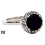 A platinum sapphire and diamond halo cluster ring, central claw set sapphire, diameter 7mm, within a