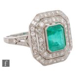 A platinum emerald and diamond cluster ring, claw and collar set emerald cut emerald within a