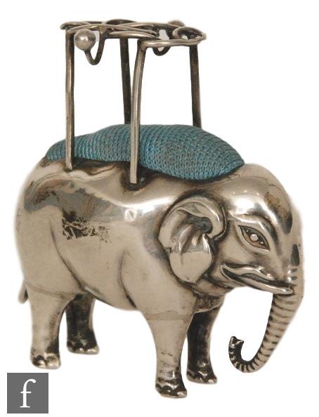 An Edwardian pin cushion modelled as a standing elephant with a pierced wire work howdah with two