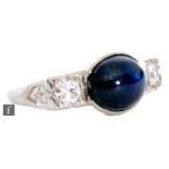 A 14ct white gold sapphire and diamond three stone ring, central oval cabochon collar set