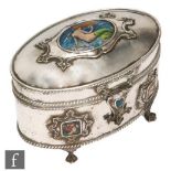 An Arts & Crafts oval white metal casket with enamel panel highlights of two maidens to the front