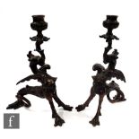 A pair of early 20th bronze winged griffin candlesticks resting on serpent tails and splayed paw
