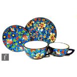 A Longwy teacup and saucer decorated with stylised flowers and foliage against a blue ground,