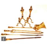 A set of three brass fire irons, a similar poker and a pair of matching fire dogs.