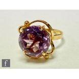 An 18ct single stone amethyst ring, circular claw set stones, diameter 14mm, to a scroll head and