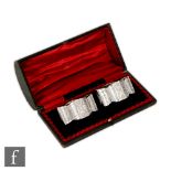 A cased pair of hallmarked silver oval shaped napkin rings each with engraved foliate decoration,