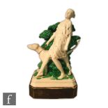 A 1930s model of a lady walking her dog, stood before green foliage, all to a painted black pedestal