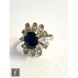 An unmarked white gold sapphire and diamond cluster ring, central oval claw set sapphire within a