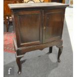 An oak double door cupboard on stand, raised to cabriole front legs and bearing an ivorine trade