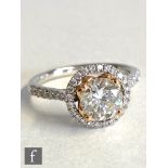 An 18ct white gold diamond halo ring, the central rose gold, claw set solitaire weight approximately