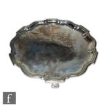 A hallmarked silver circular salver of plain form with stepped border and raised on three scroll