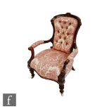 A Victorian mahogany framed elbow easy chair, upholstered in pale red leaf button back design, on