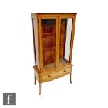 An Edwardian light mahogany two door display cabinet enclosed by a pair of glazed doors over a