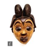 An African Punu style mask, possibly Gabon, carved coiffured hair crowning the face with exaggerated