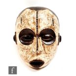 An African tribal mask, in an oval form decorated with carved stylised features outlined in black