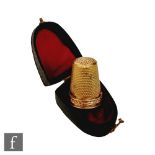 A cased gold thimble decorated with a band of flowers, unmarked, tests as 14ct.