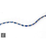 A modern 14ct white gold sapphire and diamond bracelet comprising twenty four oval claw set