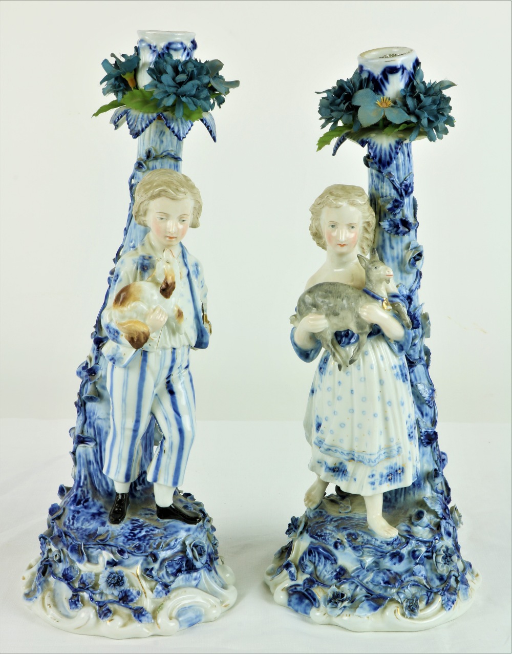 A pair of blue and white Sitzendorf Candlesticks, one of young girl holding a kid goat,