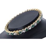 Emerald and diamond hinged bangle, with thirty-eight alternating oval set stones in yellow metal,