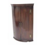 George III mahogany bowfront hanging corner cupboard, with crossbanded double doors enclosing
