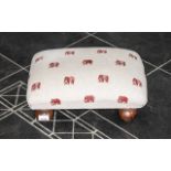 Small Footstool raised on four ball feet and upholstered in beige with red elephant print.