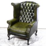 A traditional style wing-back easychair, upholstered in close studded green leather, on short