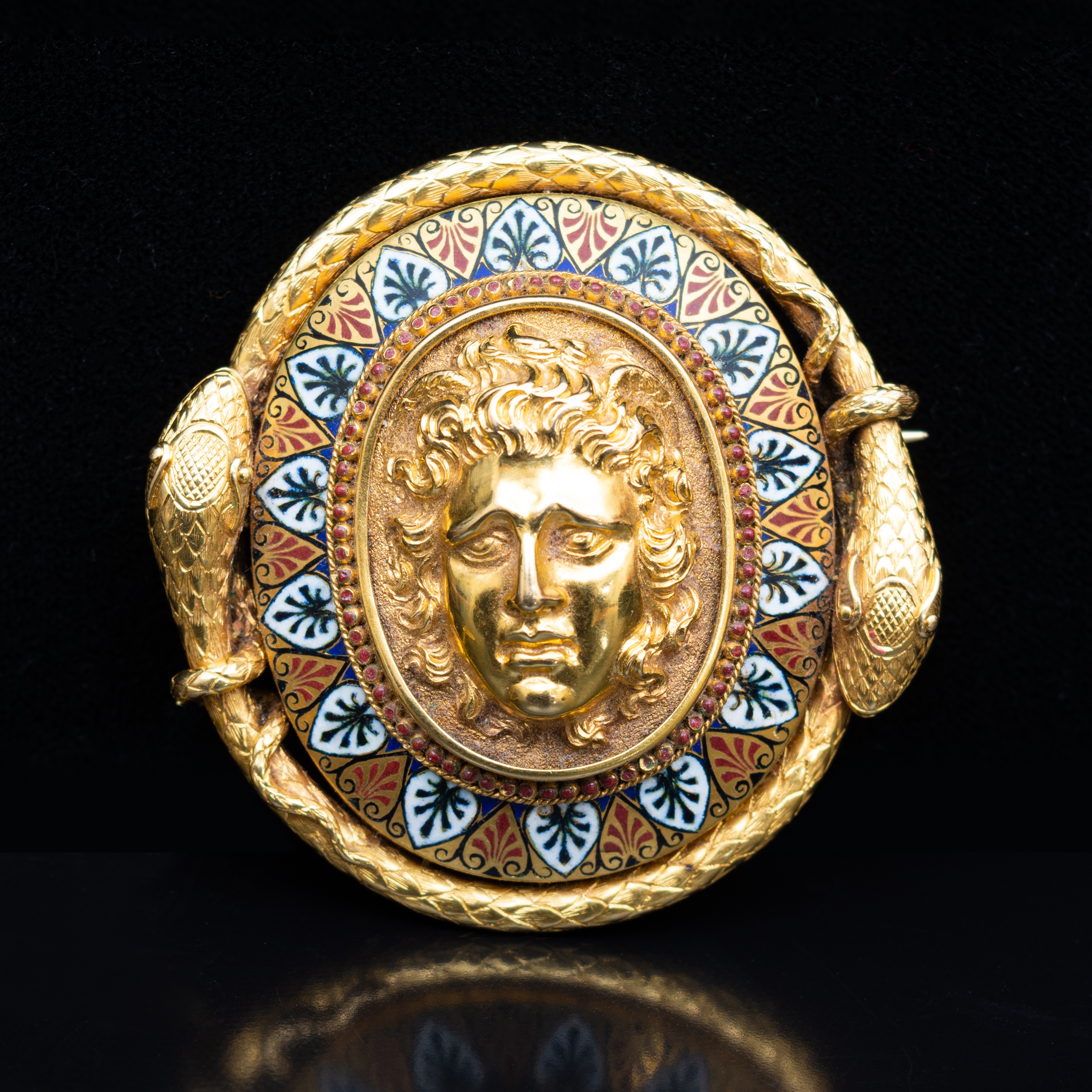 A late 19th Century yellow metal and enamel oval brooch, with a central mask in high relief.