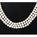 A three row cultured pearl necklace with a diamond and emerald clasp.