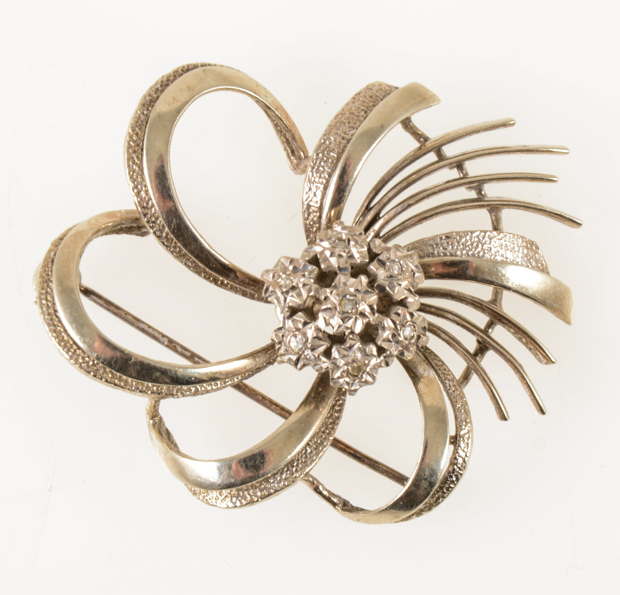 A white metal diamond set swirl brooch.