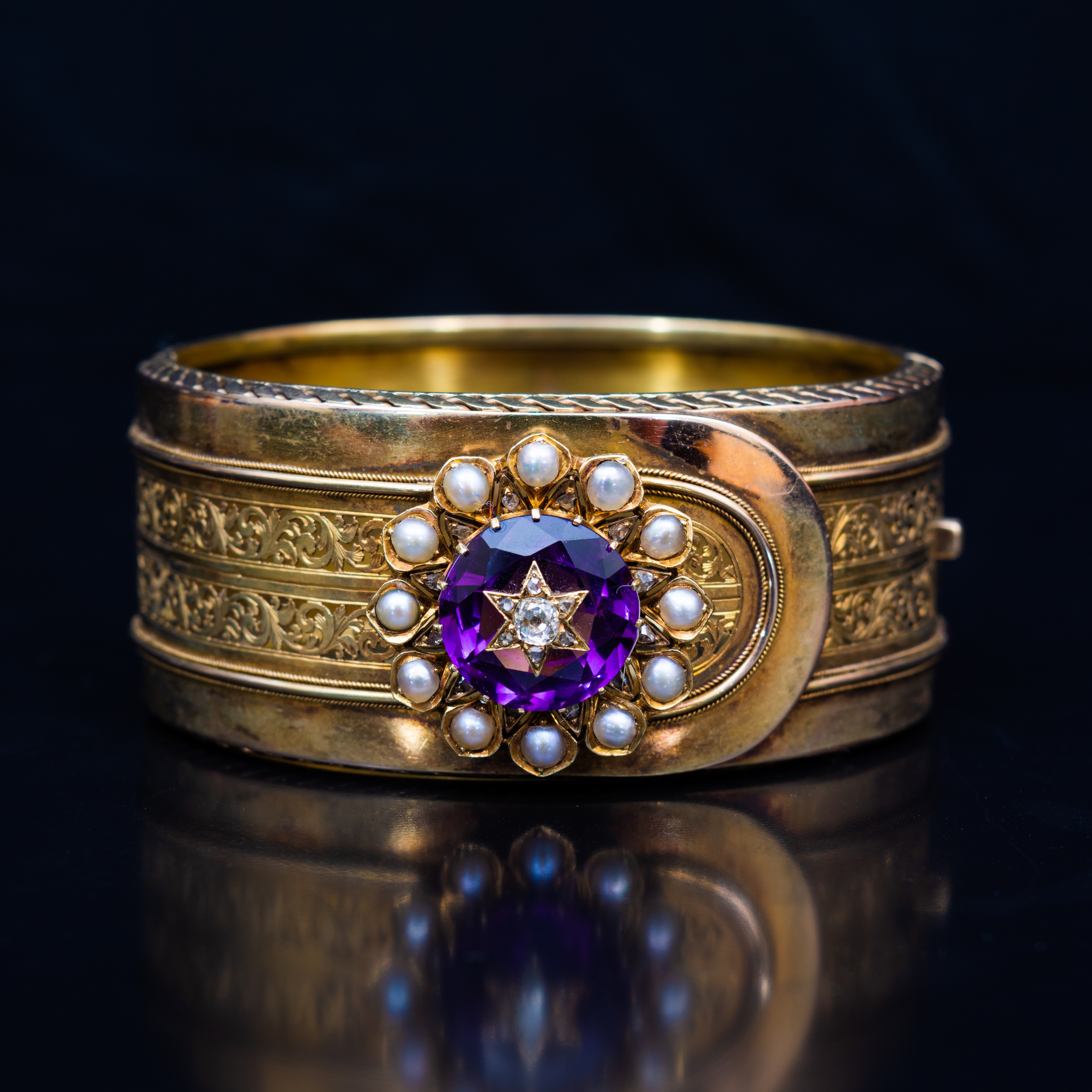 A late 19th Century yellow metal bangle with an amethyst, diamond and pearl cluster.