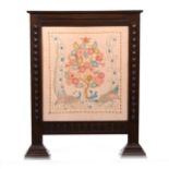 A carved oak fire screen with Arts and Crafts embroidered panel.