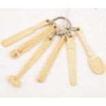A carved bone teething ring, in the shape of carpenter’s tools, a club and a cricket bat, 9cm.