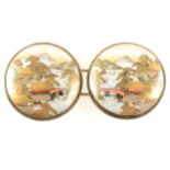 A pair of Japanese satsuma buckles, depicting scenes of mountains.