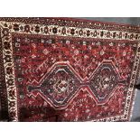 A Shiraz rug, two joined lozenge motifs on a patterned red field, border within guards, 196cm x