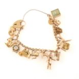 A yellow metal charm bracelet with sixteen charms plus one loose charm.