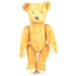 An early 20th Century straw filled teddy bear, glass eyes, hump back, jointed limbs, 28cm tall.