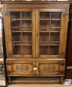 A reproduction carved and panelled oak bookcase, fitted astragal-glazed doors on stretcher base W.