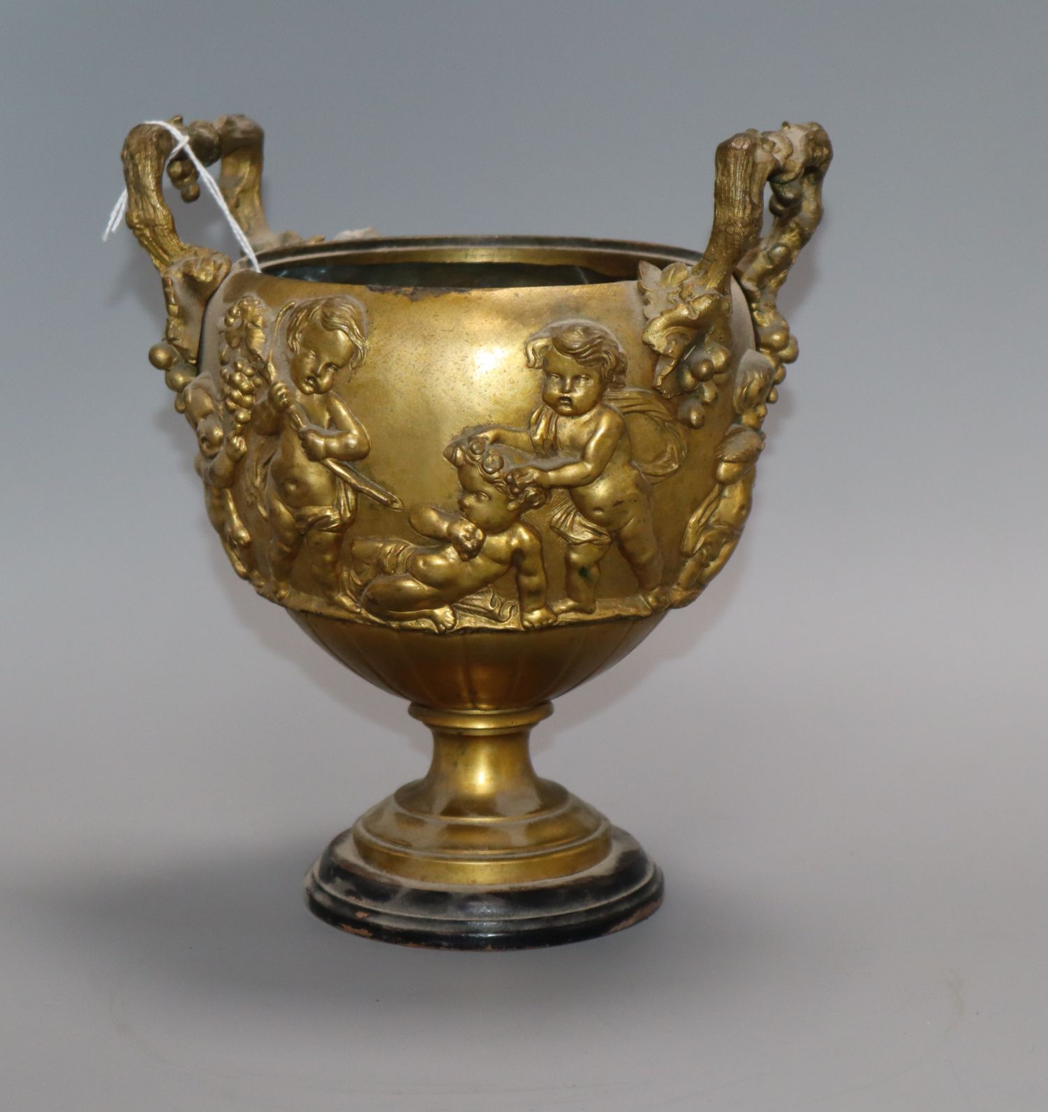 A gilt bronze two handled urn (lacking cover), depicting putti height 21.5cm