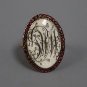 A Regency yellow metal, monogrammed ivory? panel oval mourning ring with garnet set border, size L.