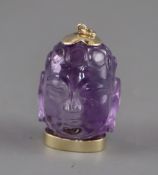 A yellow metal mounted amethyst pendant, carved as the head of Buddha, 36mm.