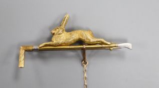 A yellow and white metal stock pin modelled as a riding crop surmounted by a running hare (tests