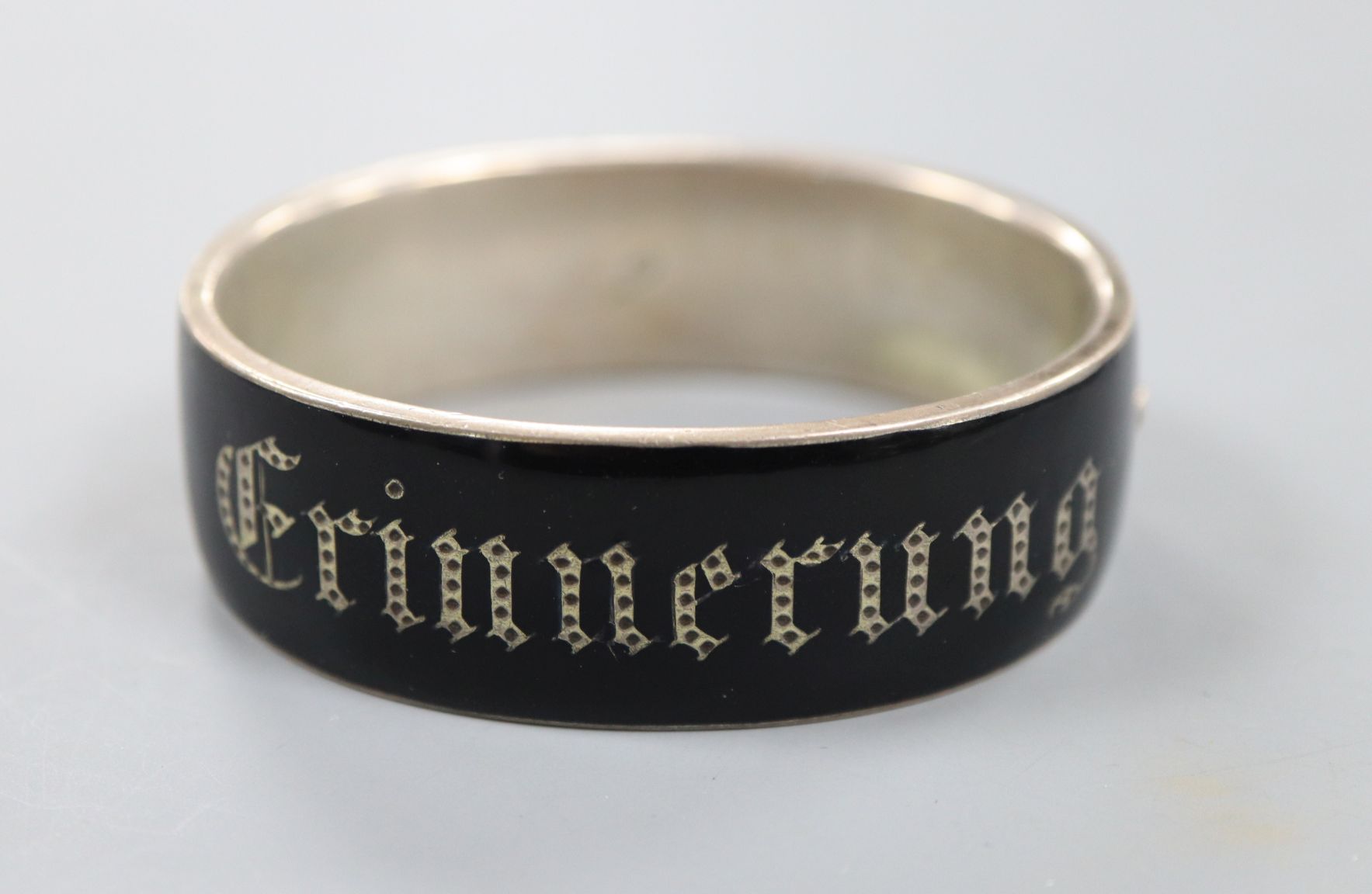 A 19th century German white metal and black enamel mourning hinged bangle, 'Erinerrung'(Memory),
