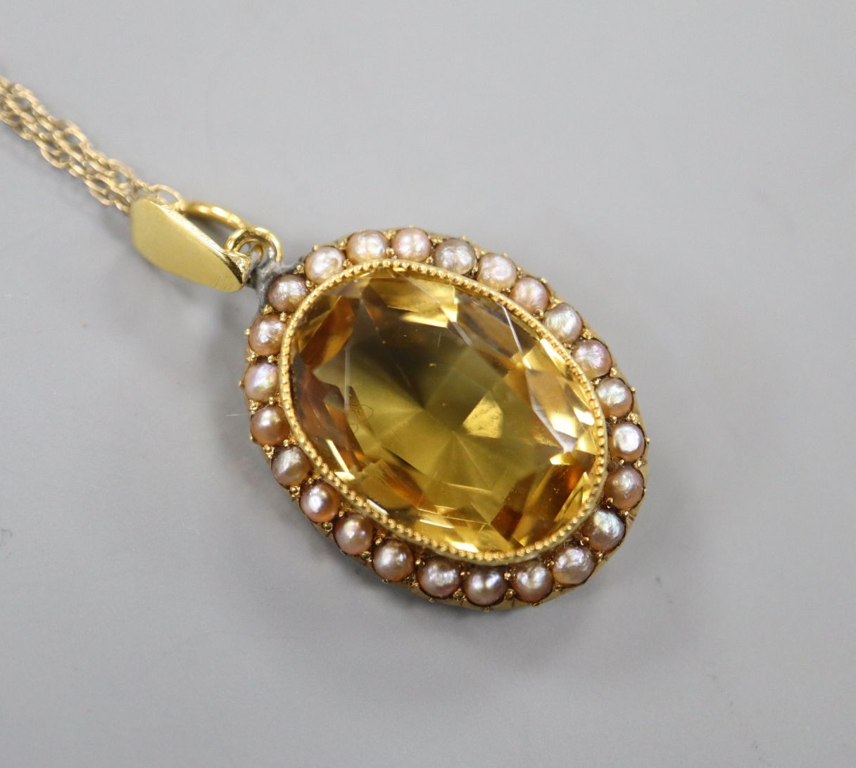 A yellow metal, citrine and seed pearl set oval pendant, on a 9ct fine link chain, pendant 21mm.
